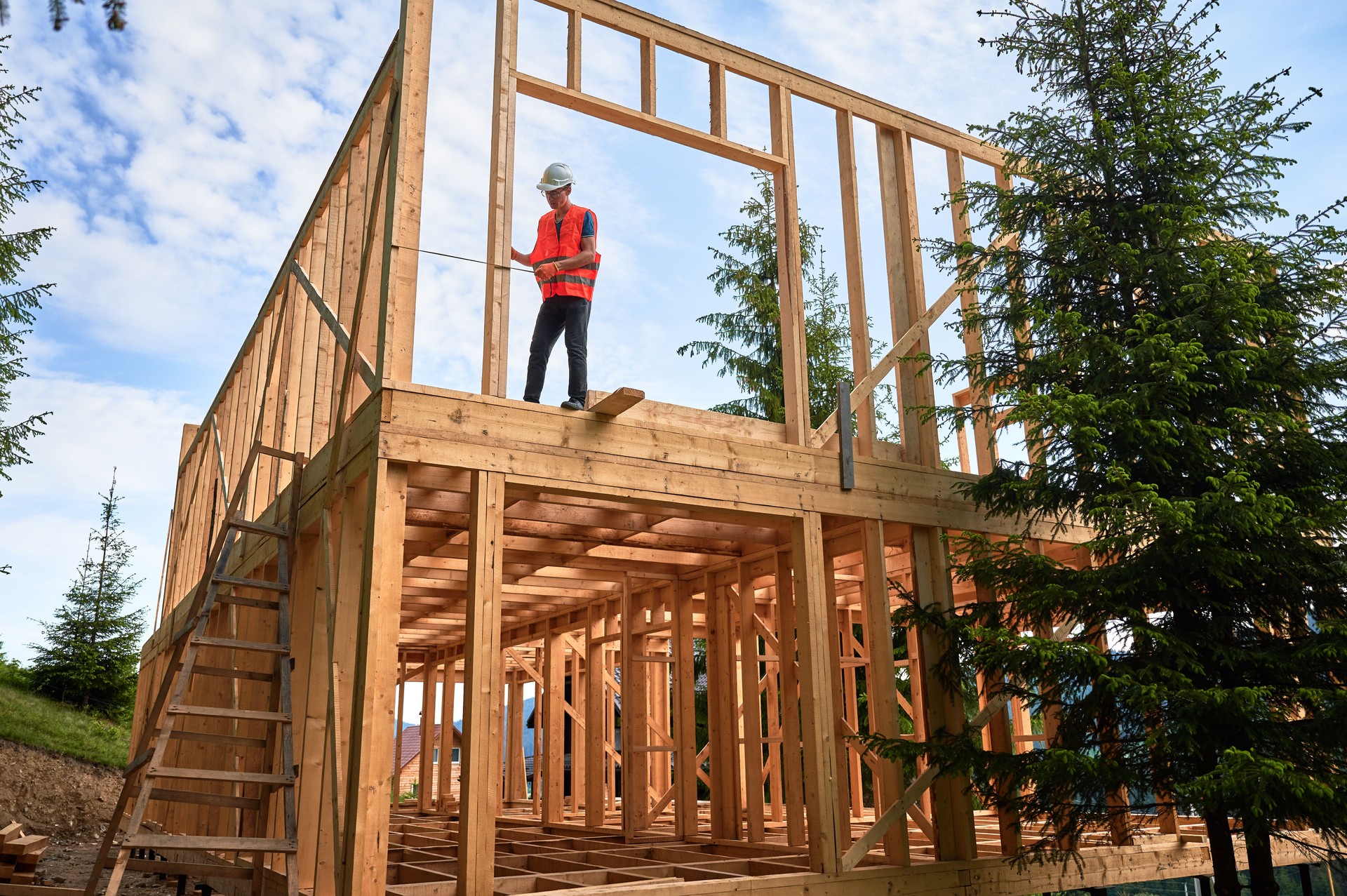Carpenter measures distance with tape measure while building wooden frame house.
